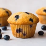Freshly baked easy blueberry muffins on a light surface with scattered blueberries in natural light