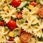 Creamy bow tie pasta salad with cherry tomatoes, peas, cucumbers, cheddar cubes, and red onion slices.