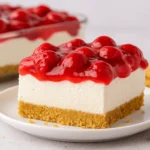 Slice of cherry delight dessert with a graham cracker crust, creamy filling, and cherry topping on a white plate.