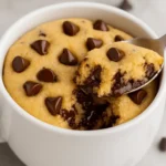 Chocolate chip cookie in a mug with melted chips, served warm in a white ceramic cup