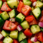 Close-up of chopped cucumber, tomato, and red onion salad garnished with fresh parsley.