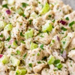 Close-up of creamy chicken salad with chopped celery, red onion, fresh parsley, and black pepper.