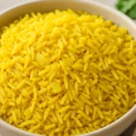 Close-up of fluffy homemade yellow rice in a white bowl, garnished with sautéed onions.