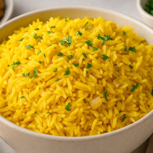 Bowl of yellow rice garnished with fresh parsley, served on a neutral table setting.