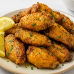A plate of crispy baked lemon pepper chicken wings garnished with chopped parsley and served with lemon wedges.
