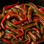 Close-up of homemade pepper steak with tender beef strips, red and green bell peppers in a savory sauce, served in a skillet.