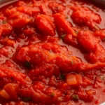 Close-up view of homemade stewed tomatoes with onions and herbs in a white bowl